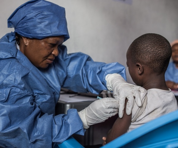 nurse in blue suit vaccinates a girl for ebola