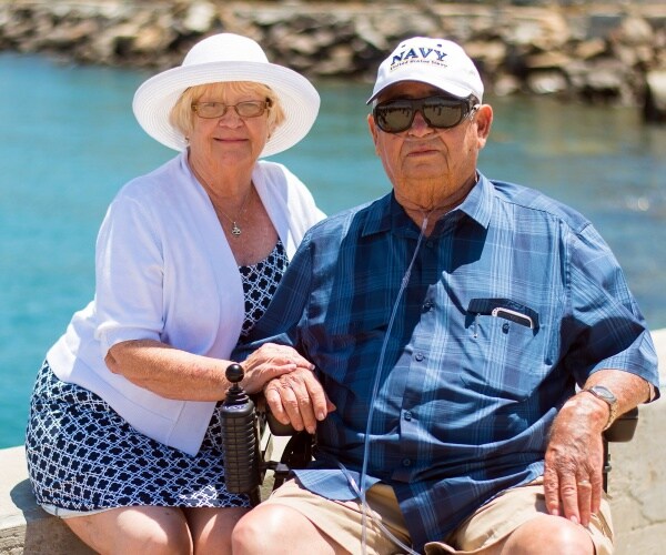 older woman sitting next to older man with oxygen outside on a sunny day