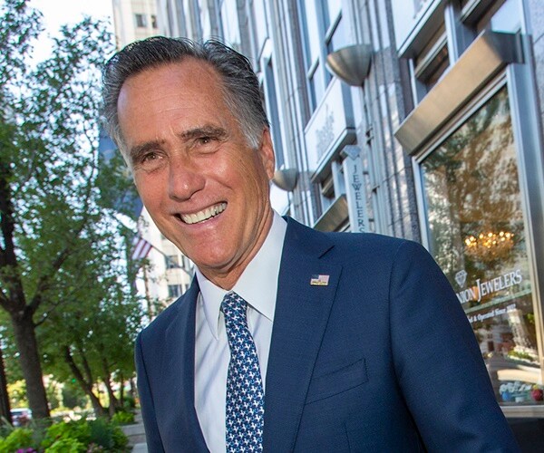 mitt romney walks across a sidewalk