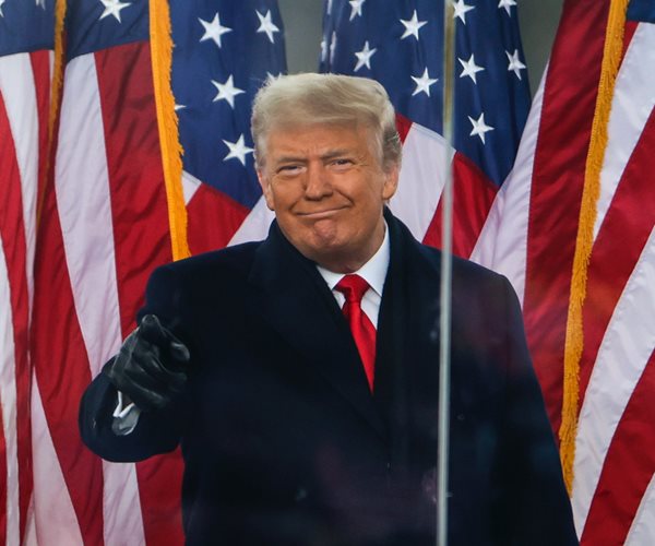 trump in a black coat standing in front of american flags