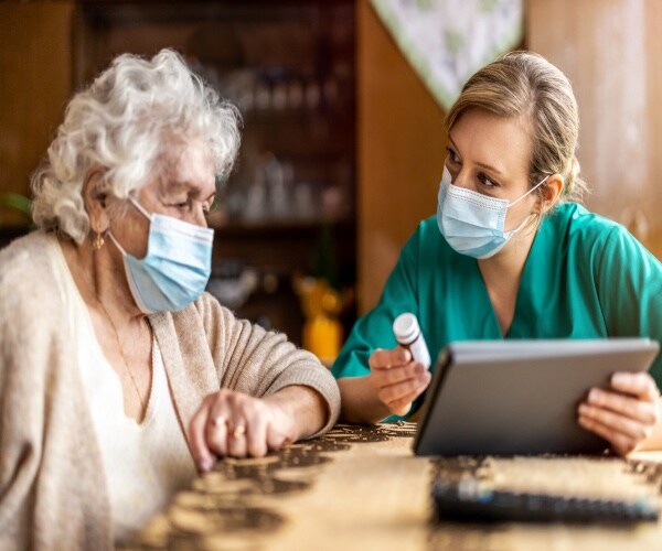 A nurse in scrubs going over medications with an older woman in her home