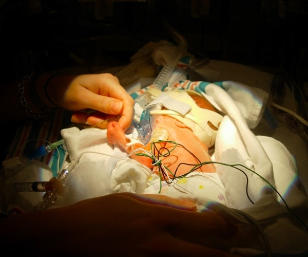 premature baby in hospital with lots of medical equipment holding finger of mother