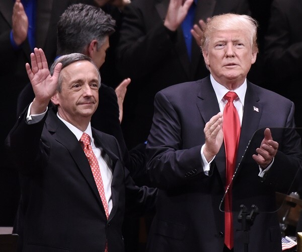 pastor robert jeffress, waving his right hand high in the air, is seen on stage with president donald trump