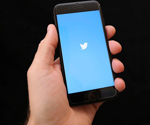 a man holds a smartphone with the twitter app logo on it