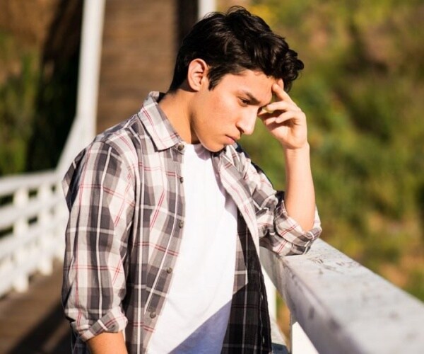 teenaged boy looking upset and standing on a bridge