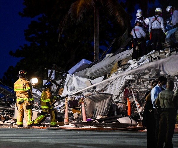 rescue workers stand in rubble of collapsed buiding