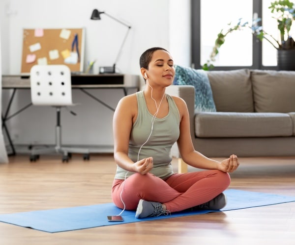 woman sitting on floor listening to music or meditation through earbuds through smartphone