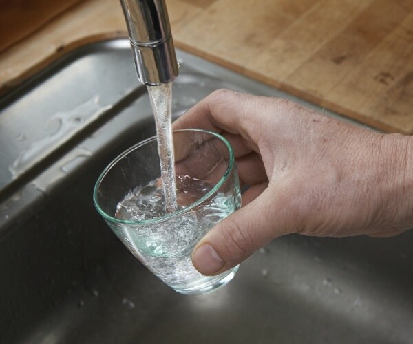 man holds glass under running faucet to get water to drink