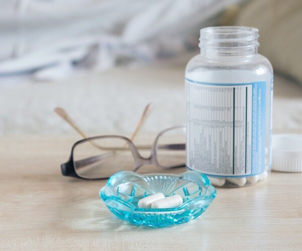 sleeping pills in glass bowl, glasses, a bottle of sleeping pills next to a bed