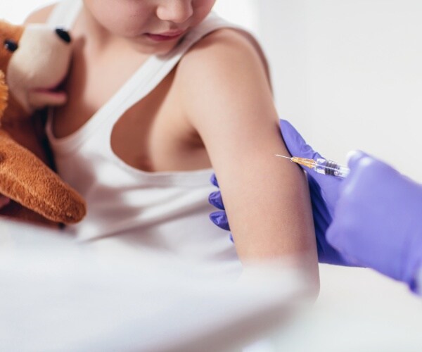 young boy holding stuffed animal getting a vaccine