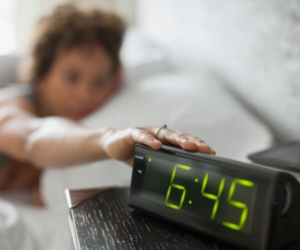 woman in bed reaching to her clock that says 6:45 to turn off alarm