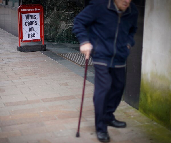 a man with a cane walks past a sign about the rising covid-19 cases in england