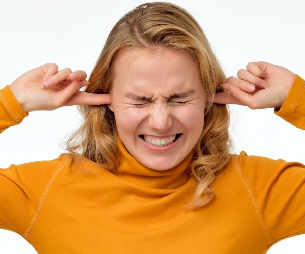 a woman with her face scrinched up and her fingers in her ears