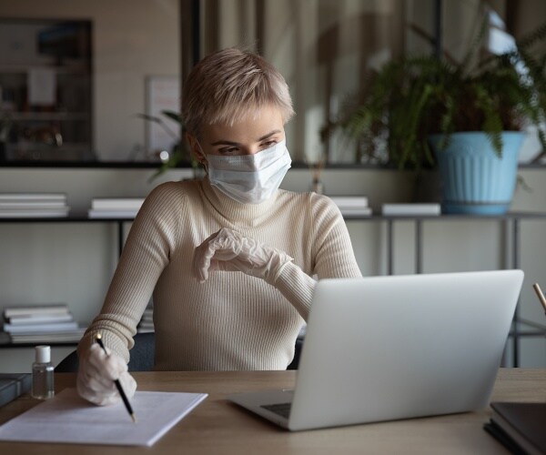 woman sits at desk wearing ppe