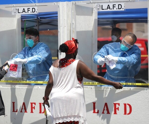 woman in long white top and red hair scarf gets tested for covid19 by man in blue protective suit and mask