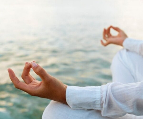 close-up of hands of person doing yoga by the water