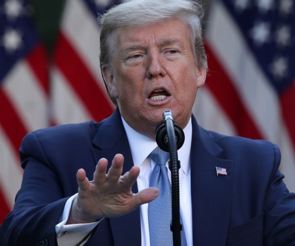 trump in a suit and light blue tie with us flag in background