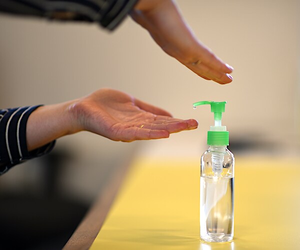 a woman presses on the top of a bottle of hand sanitizer