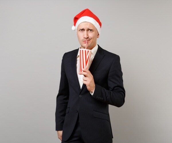 man in santa hat and suit drinking a beverage out of red and white striped soda cup