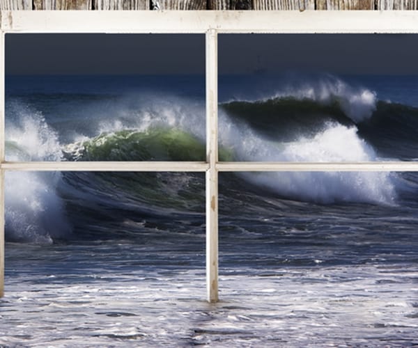 window frame of beach home with water flooding through and large wave set in background