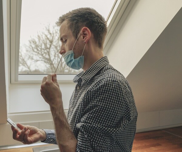 man using nasal swab to collect sample while holding the at-home COVID test