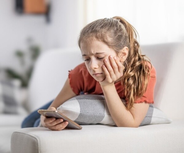 teenaged girl laying on couch and scrolling on her phone