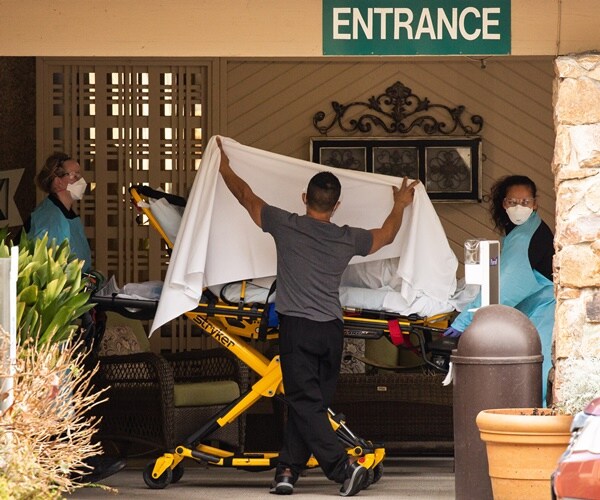 a man holds a sheet protecting a patient being rolled into an ambulance with covid-19