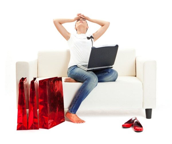 woman on couch looking stressed, with shopping packages on floor, laptop in lap