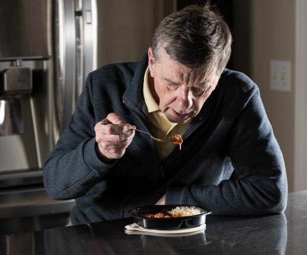 man in kitchen at night by himself eating a frozen meal heated up