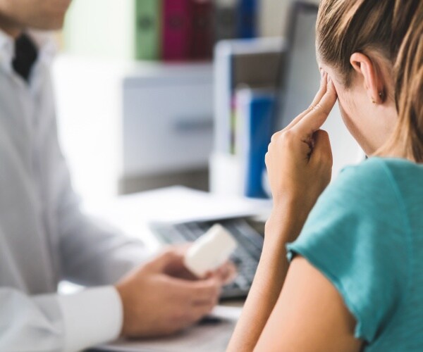 doctor holding bottle of pills, woman holding head in pain