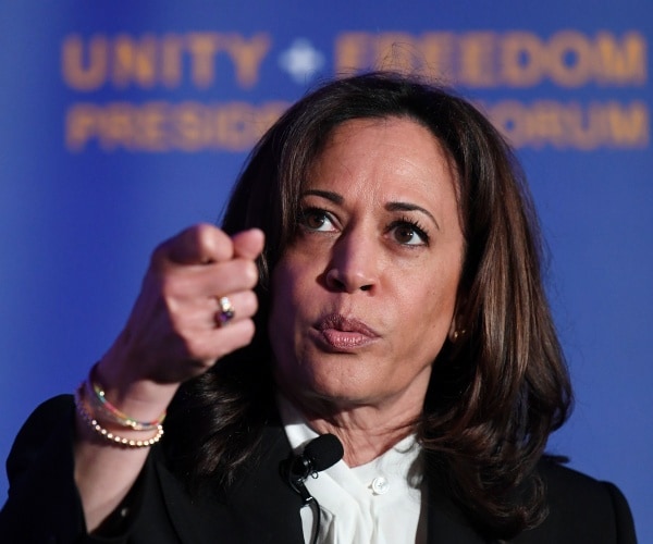 kamala harris in a white top and black coat is shown speaking