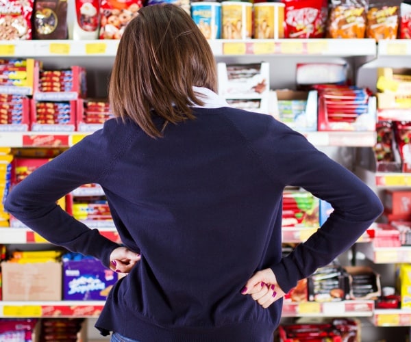 woman in supermarket with hands on hips looking at foods on shelves