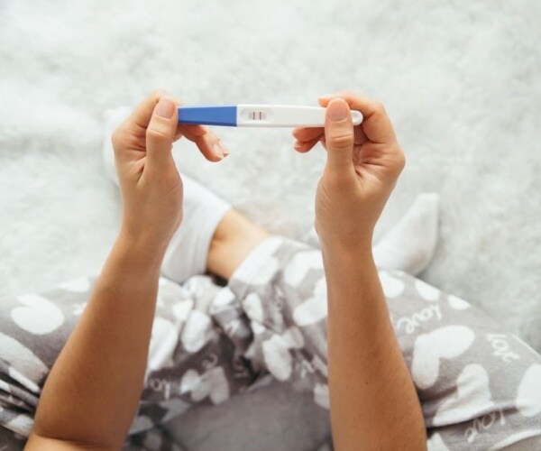 woman sitting cross-legged holding a positive pregnancy test