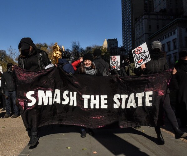 antifa activists dressed in black hold up a banner saying smash the state