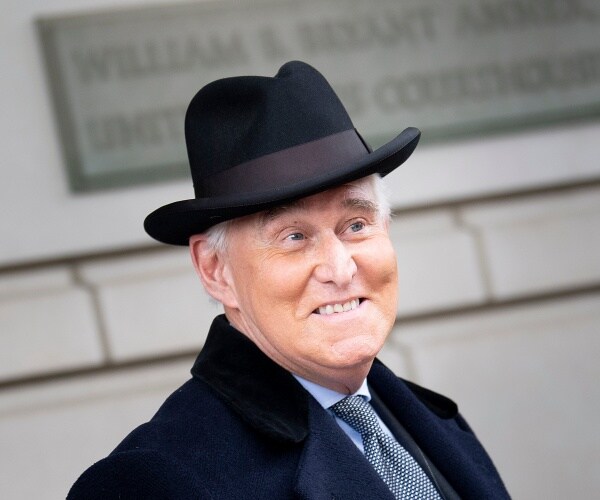 roger stone in a black coat and black bowler hat smiling