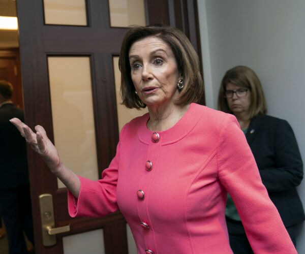 nancy pelosi gestures with her hand and is shown in a pink suit