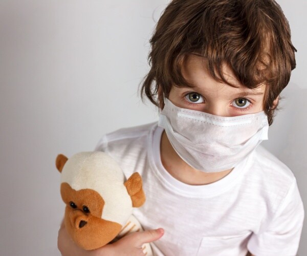 boy in mask holding stuffed animal looking worried into camera