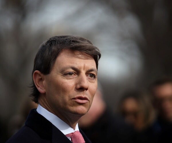 gidley in a black coat and light red tie walking outside