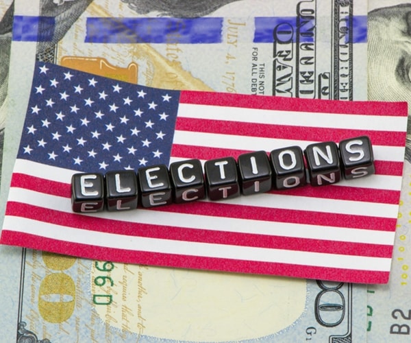 elections in white capital letters on black blocks atop usa flag and 100 dollar us bills