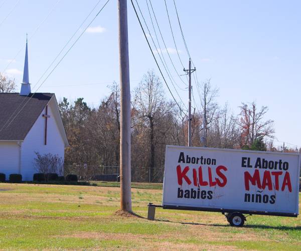 a church and a sign that reads in english and spanish "abortion kills babies"