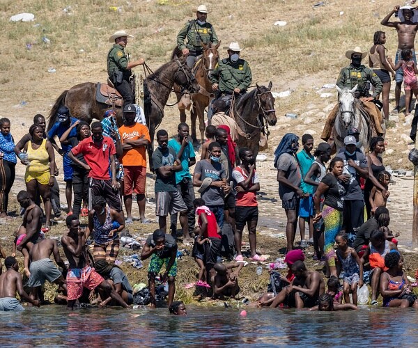 border patrols agents on horseback watch migrants cross river