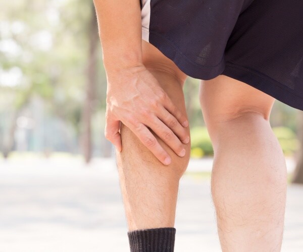 man walking outside and holding back of leg in pain