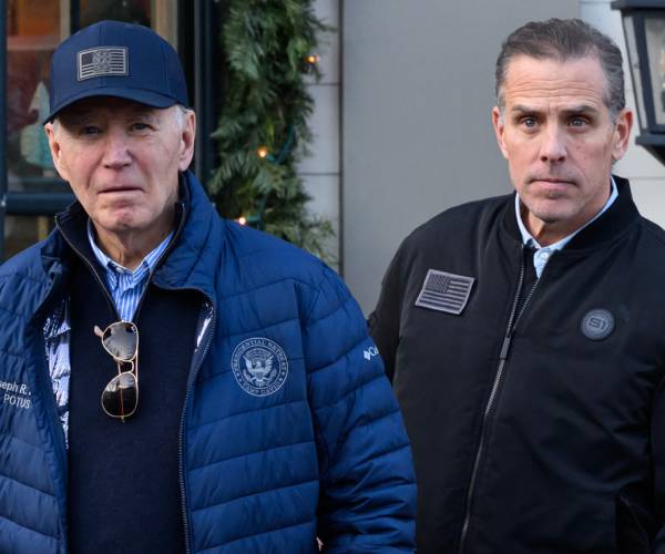 joe and hunter biden in coats with joe wearing a presidential seal on his coat and a cap with an american flag patch