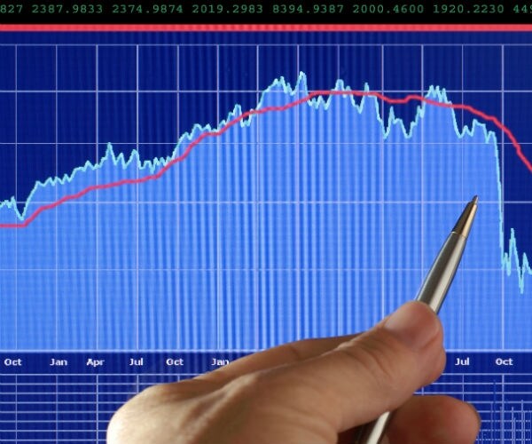 Man with pen pointing to blue chart with white writing and downward falling slope