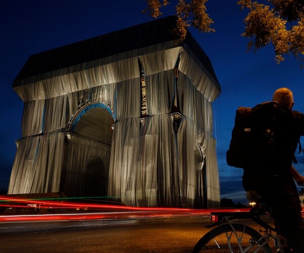 cyclist looks at arc de triomphe wrapped in fabric