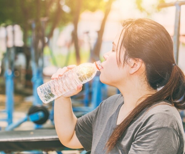 sweaty woman drinking water outside on a hot day