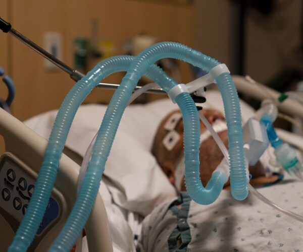 patient lies in a hospital bed with a ventilator