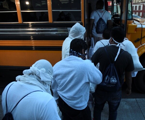 migrants being deported line up to get into a school bus