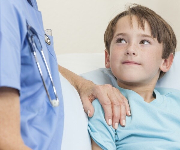 young boy in hospital bed, healthcare worker with hand on his shoulder