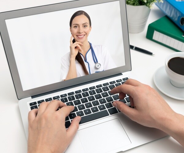 person looking at laptop with doctor on screen for telemedicine appointment